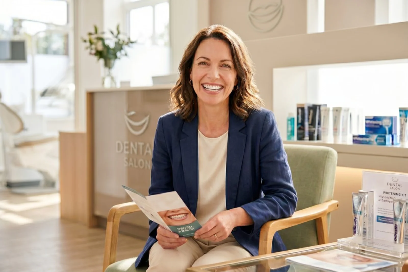 Smiling patient seated in the Dental Salon reception area holding a brochure that shows a bright, even smile.